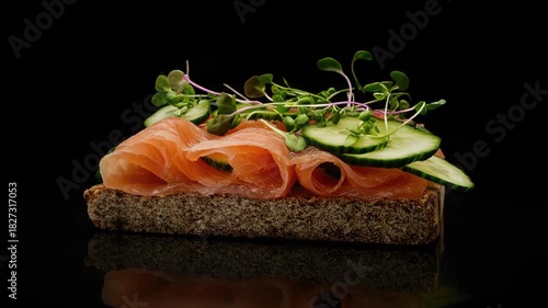 Smoked salmon slices on a slice of rye bread topped with cucumber, sprouts, seeds and purple onions