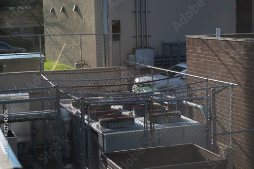 Foto Industrial Rooftop HVAC Cooling Tower and Air Conditioning Units Enclosed in a Chain-Link Security Fence on a Brick Building
