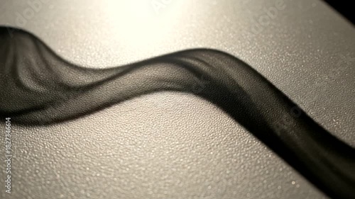 Elegant black fabric ribbon gracefully flowing across a shimmering surface with soft light