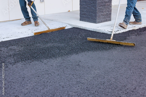 Φωτογραφία Workers use large rakes to spread freshly laid asphalt at busy construction site