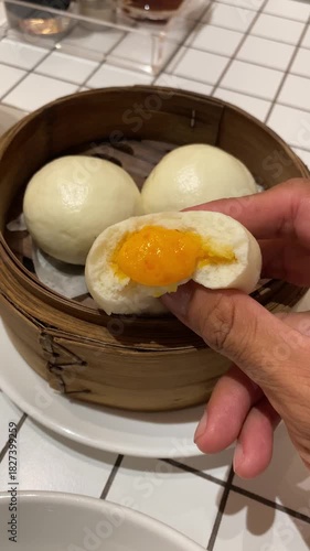 Someone hand is squeeze a Salted egg baozi or Bakpau Telur Asin placed in bamboo steamer. Steamed chinese dumpling dim sum. Authentic typical chinese food. Vertical video footage