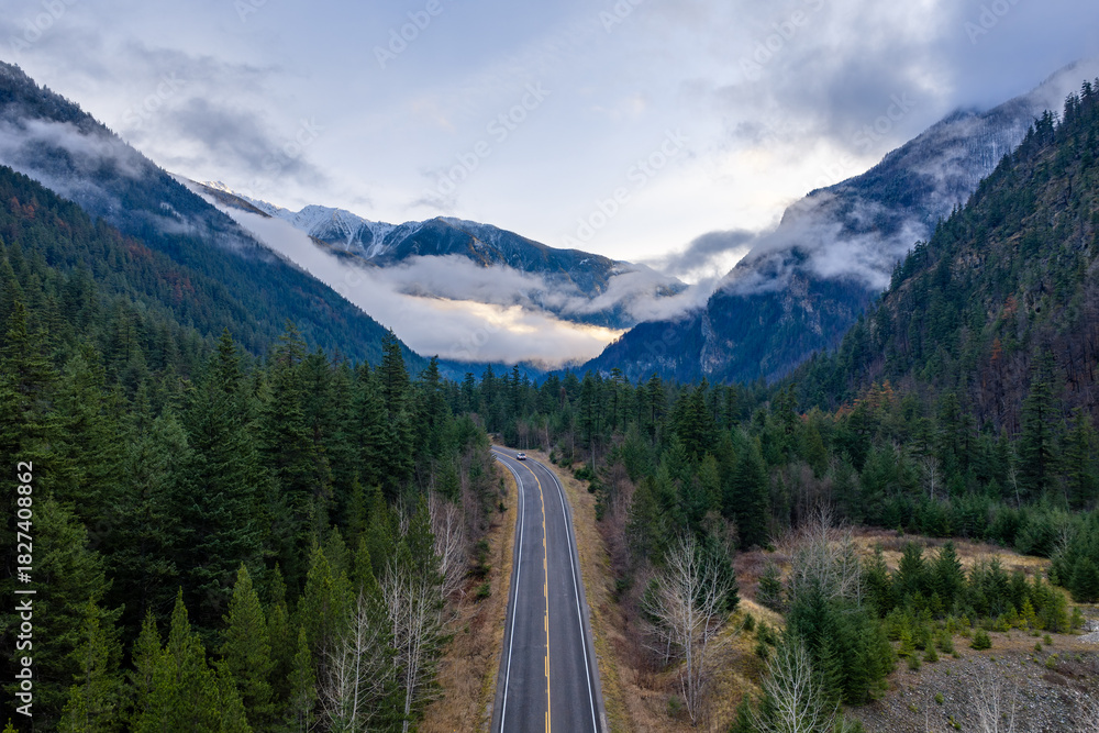 Fototapeta premium Scenic Mountain Road Through Conifer Forest Toward Snow-Capped Peaks in BC, Canada