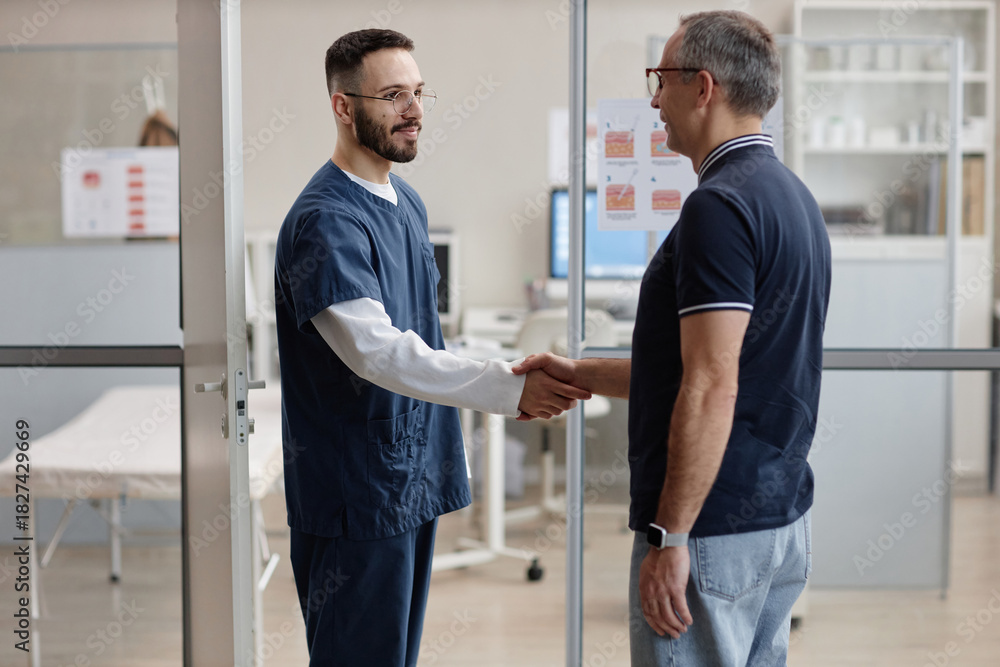 Obraz premium Male dermatologist greeting middle aged Caucasian man with handshake in medical office, both standing near examination room, discussing skin health during patient appointment