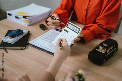 A smiling woman hands over car keys and receives payment during a vehicle purchase transaction at an office desk.