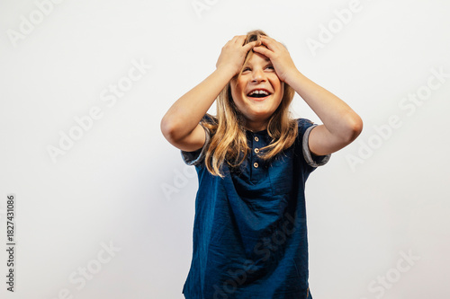 Child laughing with hands on head joyfully.