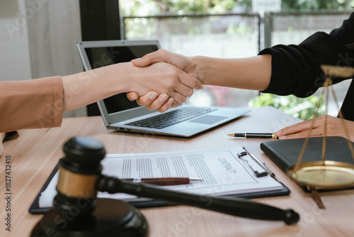 Two professional women discussing legal documents at an office desk, reviewing contracts with a laptop and gavel nearby.