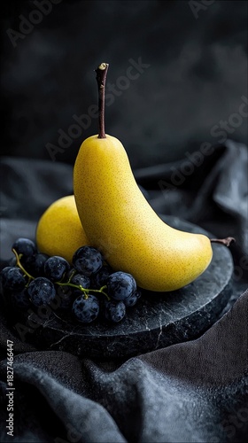 A still life composition featuring a ripe yellow pear and a cluster of dark grapes resting on a dark marble plate. The arrangement is set against a dark, textur