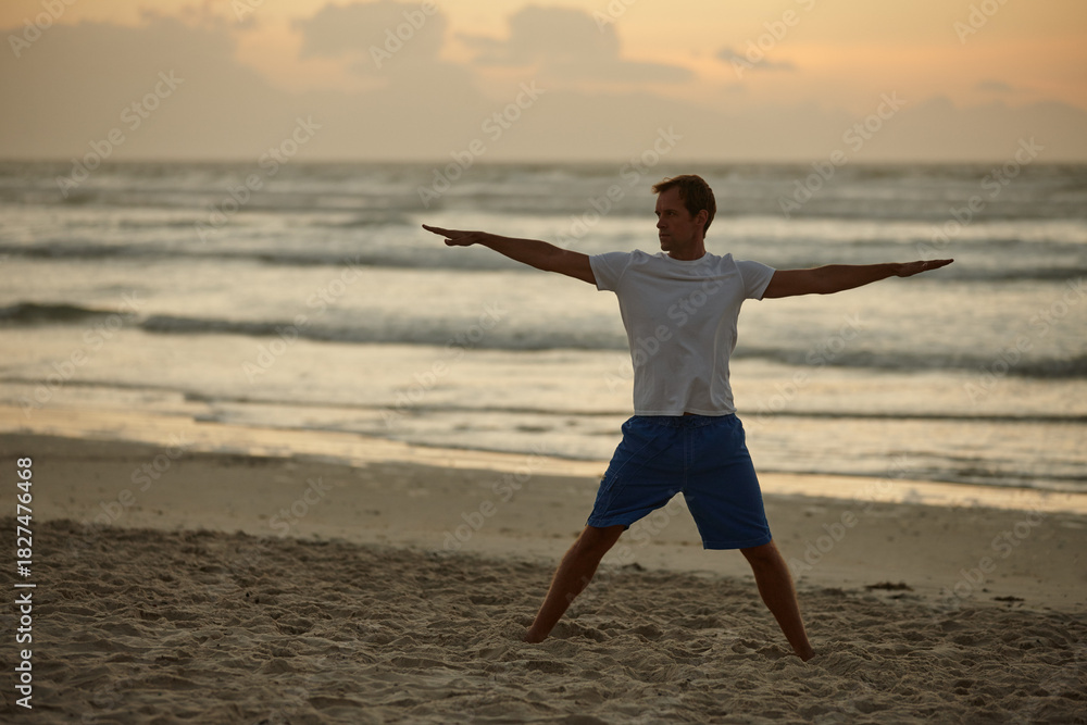Fototapeta premium Man, stretching and exercise for yoga on beach for mindfulness, spiritual healing and zen. Person, sunset and space with warrior pose for holistic balance, inner peace and self care goals on seashore