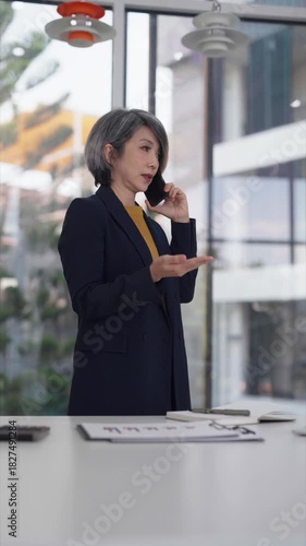 Asian older businesswoman professional working modern office contemplating strategy planning laptop review documents desk workspace serious focus business solution