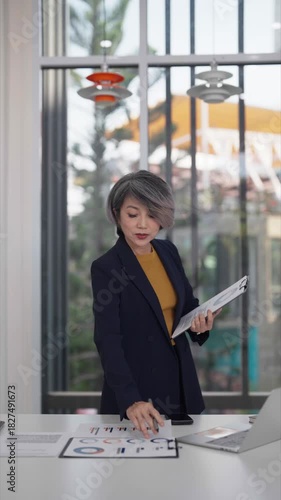 Asian older businesswoman manages schedule making phone call office setting ensuring productivity meeting critical deadlines