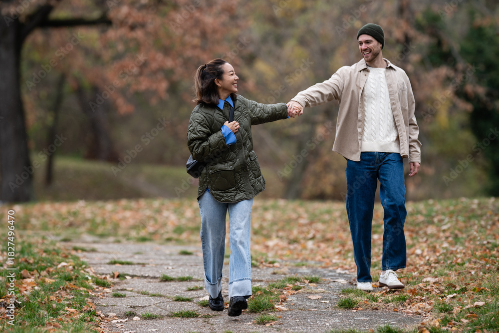 Fototapeta premium Happy multiethnic couple holding hands walking in autumn park