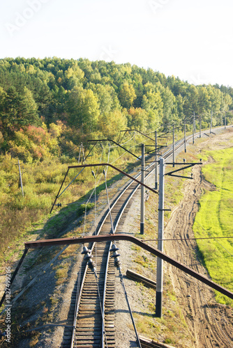 Siberian forest and empty railroad tracks with overhead catenary system stretching into distance. Symbolizes remote transportation routes, regional connectivity and sustainable mobility infrastructure