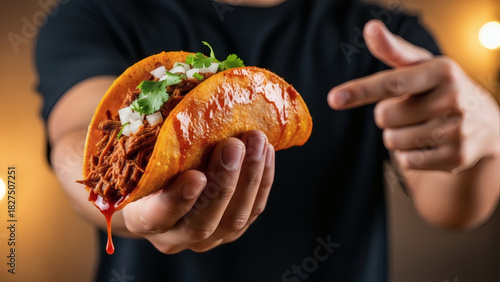 Hand Holding and Pointing at Birria Taco with Sauce Dripping. Shredded Beef Quesa Taco Being Offered. Delicious and Juicy Authentic Mexican Food with Warm Background Lighting.