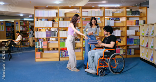 Indian young adult male man sitting wheel chair use tablet take part group study speak show screen share new ideas indoor gen z pupil teen girl boy hold book talk library college place