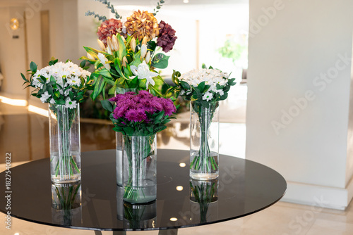 Three vases with colorful flowers on a black table in a bright indoor setting. The arrangement includes white, purple, and green flowers.