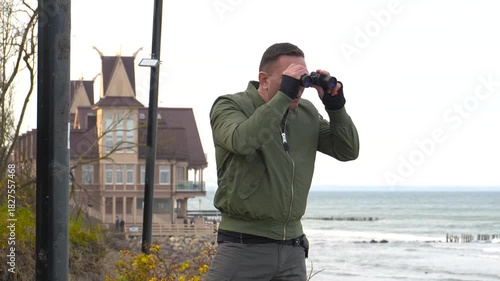 A man watches the beach through binoculars. The man blows a warning whistle at violators.