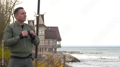 A man observes the situation on the beach through binoculars. A man observes the situation on the seashore through binoculars.