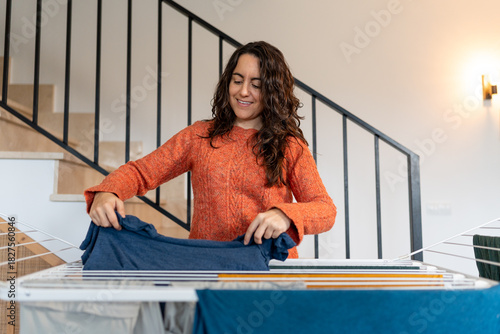 Quadro em tela Woman folding clean laundry on drying rack at home