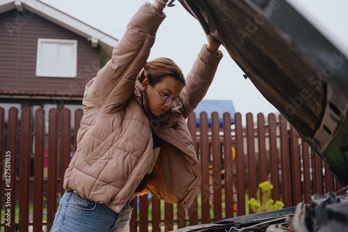 A young woman discovers engine trouble in her car, trying to understand the problem while calling for help. Authentic moment of vehicle breakdown and problem-solving