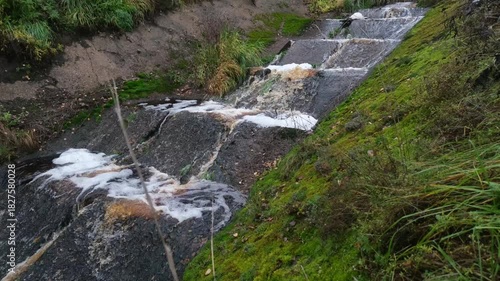 Stormy sewage flows down a cascade of concrete slabs with foam and hissing. A muddy stream