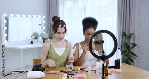 asian teenage girl holding mirror smiling while african american teenage girl holding brush during slowmotion skincare tutorial shoot at home setup showing joyful cosmetic influencer lifestyle routine