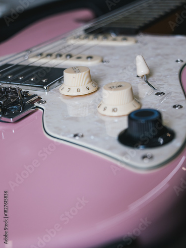 Close-up of a pink electric guitar with white pickguard and knobs. This image showcases the details of an electric guitar, highlighting its color and components