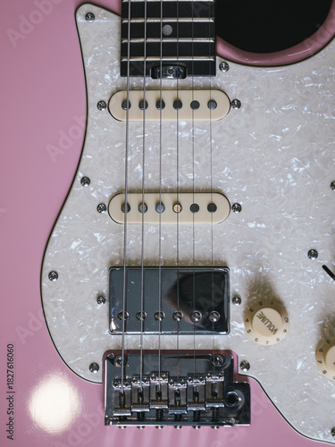 Close-up of a pink electric guitar with pearl pickguard and chrome hardware. This image showcases the details of an electric guitar, highlighting its design and components
