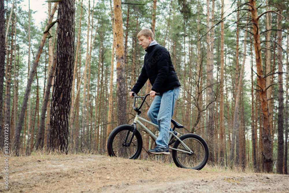 Fototapeta premium Young person on a BMX bike riding through a serene pine forest, capturing the spirit of outdoor adventure and youthful energy. Ideal for themes of nature, sport, and active lifestyle.