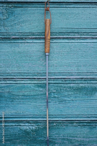 one gray long metal skewer with a brown handle lies on a green wooden table