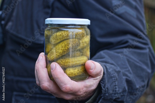 hand holding one glass jar with green canned cucumbers  in the street