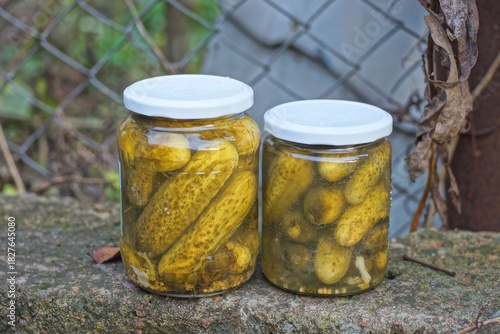 two glass jar with green canned cucumbers stand on a gray table in the street