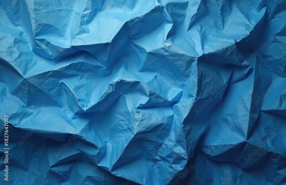 Fototapeta premium Abstract blue crumpled texture background shows many folds, creases. Wrinkled paper surface varying light, shadow, creating depth for design use. Dynamic pattern provides ample copy space for graphic