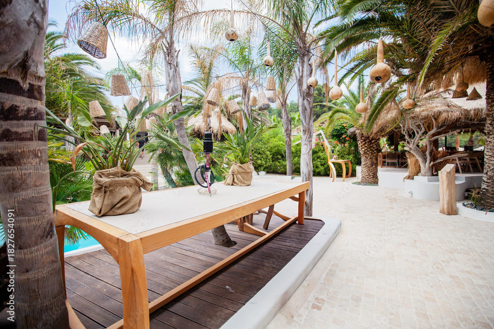 Fototapeta premium Tropical resort lounge with pool, palm trees, cushions, and thatched roofs