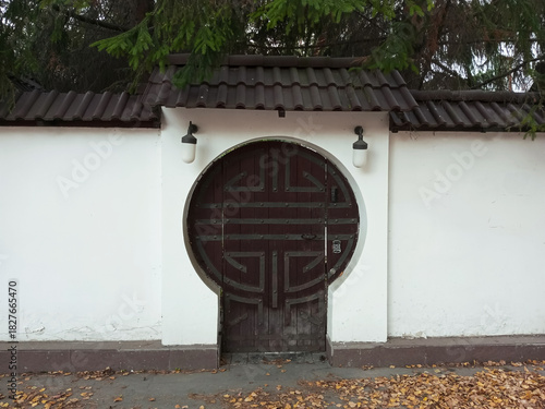 A round antique wooden door set into the wall of a plastered fence. The entrance to the courtyard of a private home.