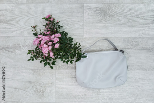 A bouquet of pink garden roses in a white leather bag lying on a white wooden background. Top view.