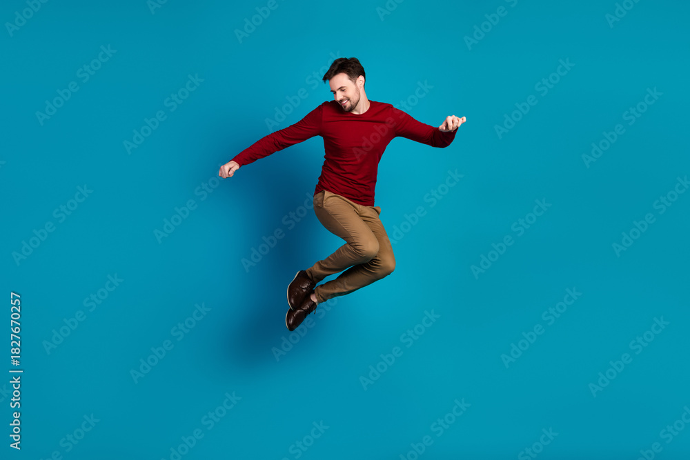 Fototapeta premium Dynamic jump by a young man in red sweater against blue background showcasing casual fashion and athletic style