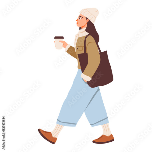 Woman walking with coffee in cozy winter outfit. Female strolling with a takeaway coffee, dressed in warm winter clothing including a beanie, jacket, wide leg pants, and tote bag.