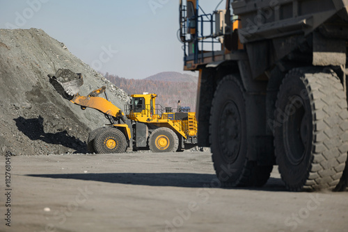 Industry Open pit mine of gold, copper, iron, magnetite ore. Big yellow mining truck at working with heavy industrial wheel loader.