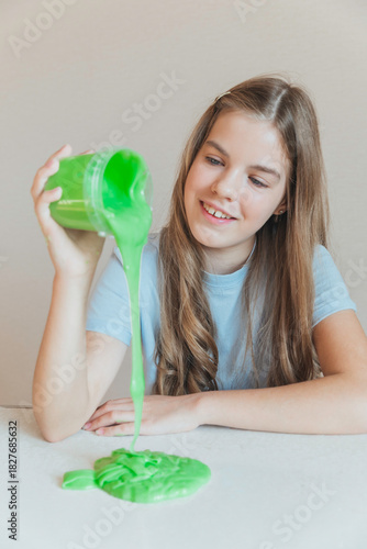 Smiling girl pouring vibrant green slime from a container onto the table. Trendy DIY and fun sensory play activity