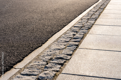 Asphalt Road Edge With Stone Curb And Concrete Sidewalk In Sunlight, Urban Street Surface Detail For Transport Infrastructure Background