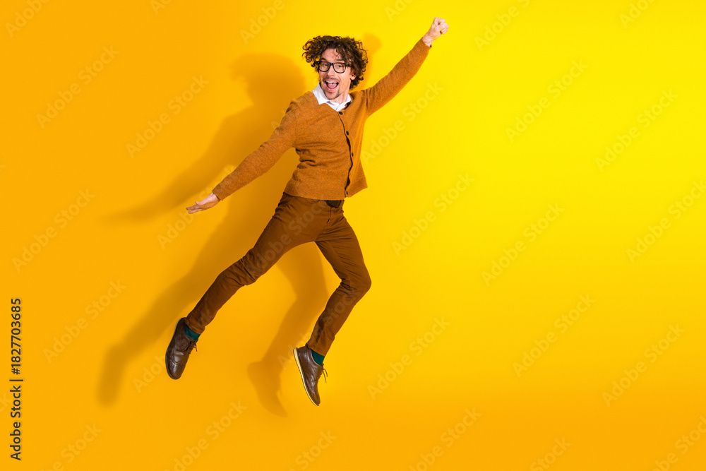Obraz premium Energetic man in mustard cardigan jumps with joy against a bright yellow background