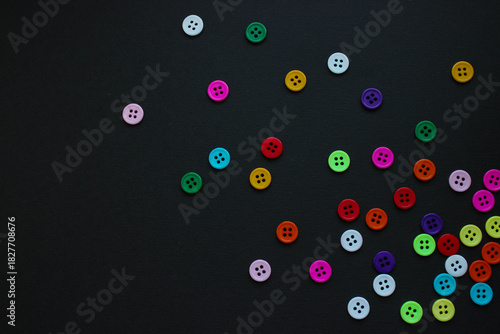 Fotografía Bright four-hole buttons in many colors scattered across a textured black background
