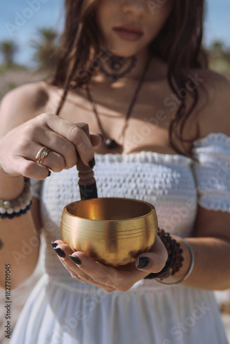 Close up woman begins to play Tibetan bowl with wooden mallet, representing sound healing and meditative focus. Concept of energy of mindfulness and the soothing vibration of inner calm