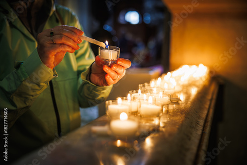 Female worshipper igniting candles in sacred interior of church. Quiet prayer symbolizing christian faith, remembrance and hope