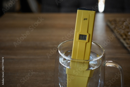 Photos Measurement of water pH level using a digital tester in a clear glass on a woode