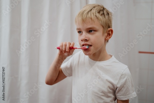 A 9-year-old boy with hearing aids brushes his teeth in the bathroom. Authentic daily routine moment showcasing independent self-care and inclusive family life