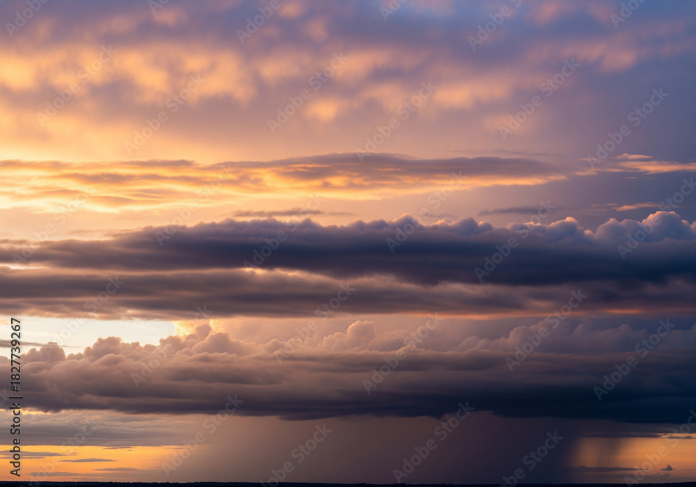 Naklejka premium Golden hour illuminates dramatic stormy clouds over the ocean, with a distant rain shower visible as the sun sets, creating a breathtaking atmospheric landscape painting