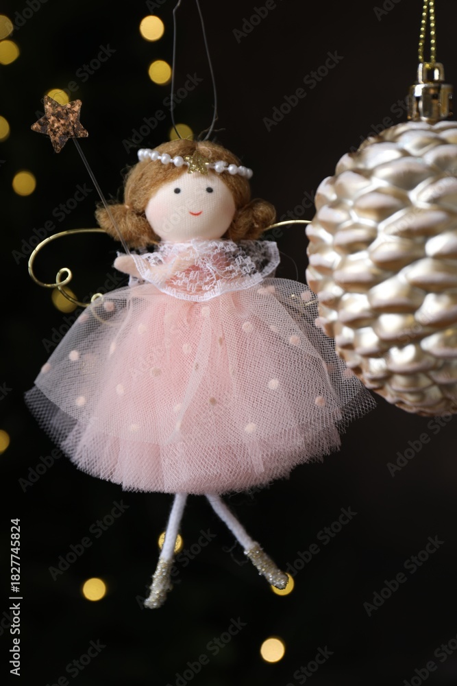 Fototapeta premium Beautiful Christmas bauble and fairy doll hanging against black background with blurred lights, closeup