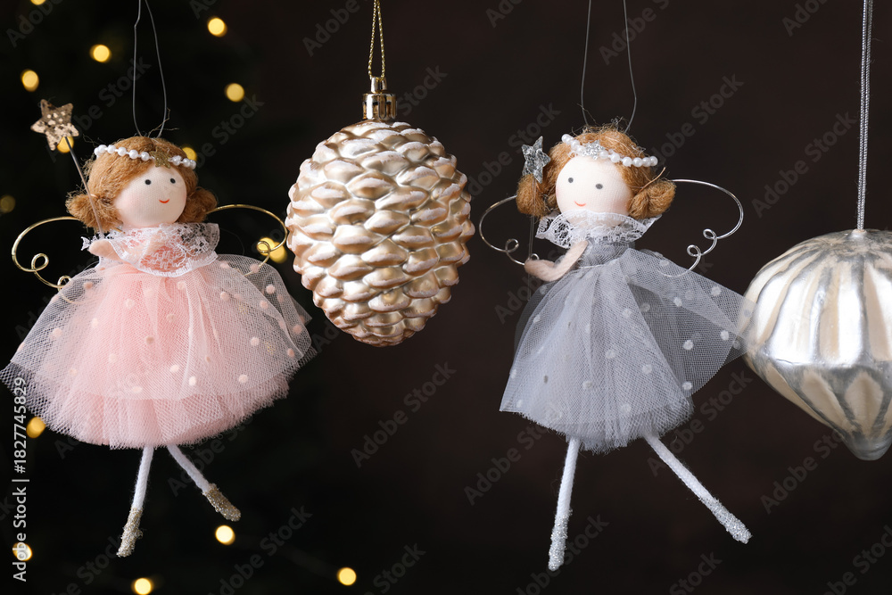 Fototapeta premium Beautiful Christmas decor and fairy dolls hanging against black background with blurred lights, closeup