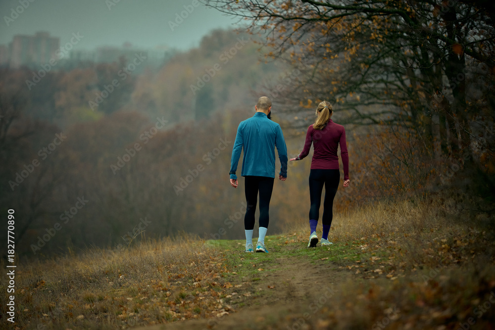 Fototapeta premium Couple walking cool-down path in misty autumn forest after trail run. Concept of corporate wellness, burnout-relief storytelling, mental health breaks, lifestyle and seasonal content.